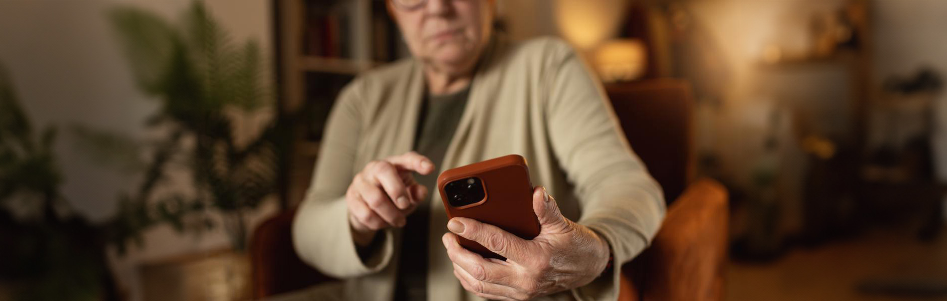Older woman using a smartphone at home, focusing on the screen with one hand pointing.
