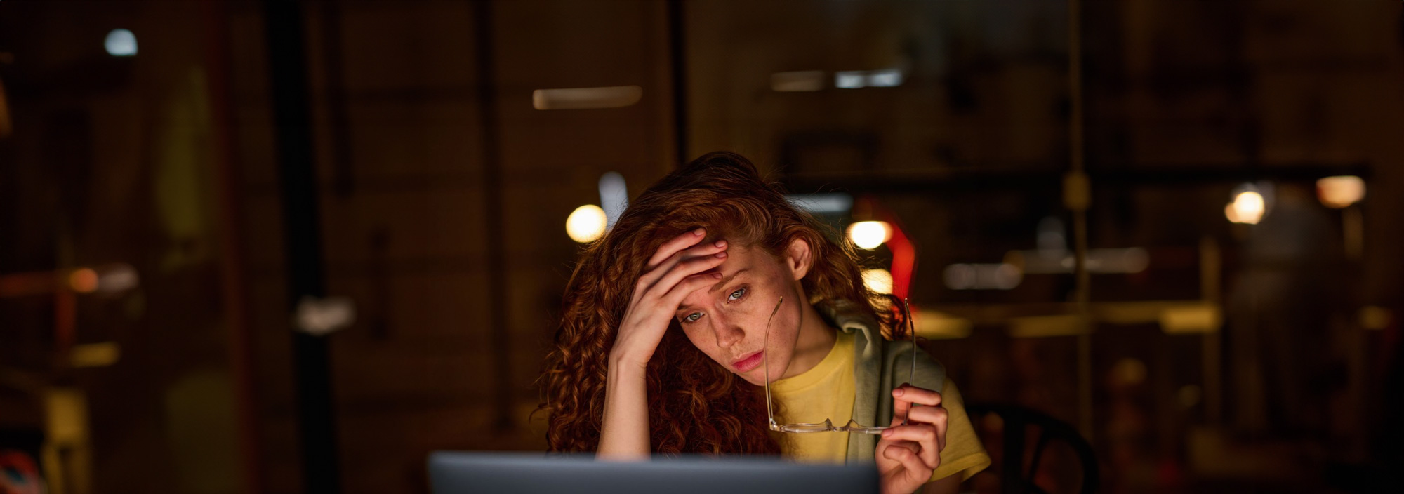 Stressed woman holding her head while looking at a laptop screen in a dimly lit room