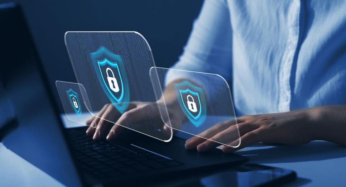 A person typing on a laptop with digital lock icons and shield symbols representing cybersecurity and data protection.